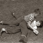 1950s Two Boys Wear Tee Shirts Blue Jeans Playing Rough Fighting Wrestling On The Grass
